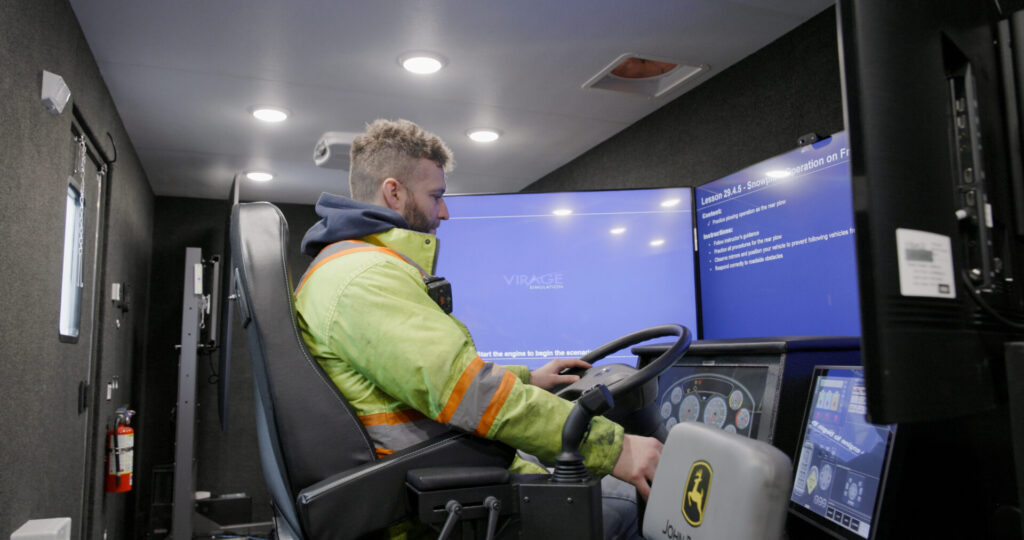 Man on Virage snowplow simulator inside the RoadShow Operator Classroom Trailer