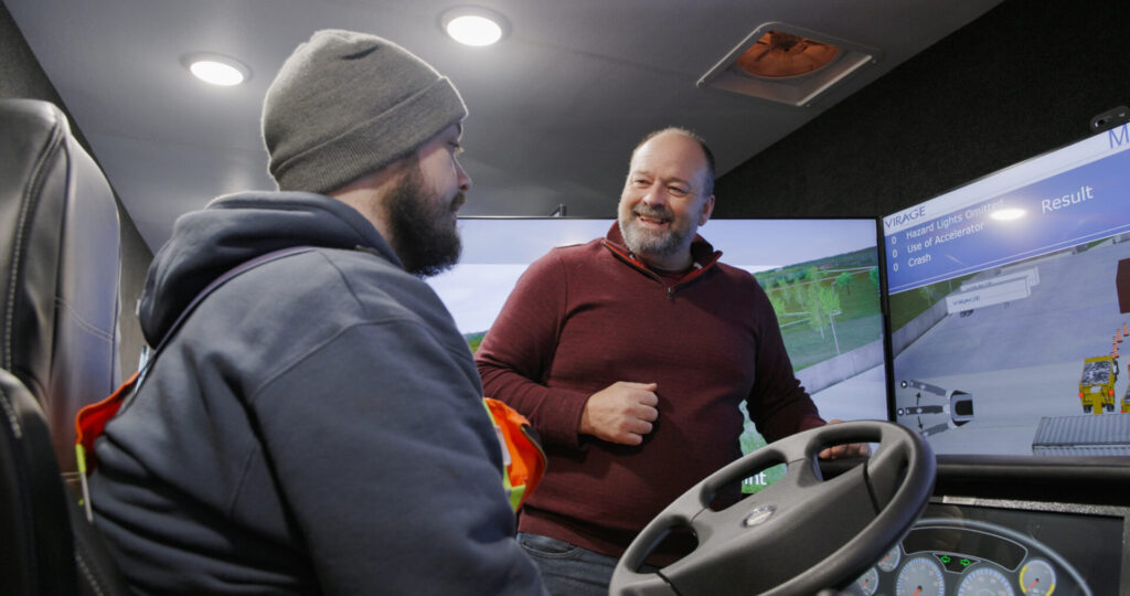 Instructor teaching man on Virage snowplow simulator in side the RoadShow Operator Classroom